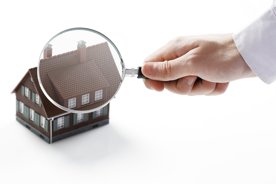 Concept image of a home inspection. A male hand holds a magnifying glass over a miniature house.
** Note: Shallow depth of field